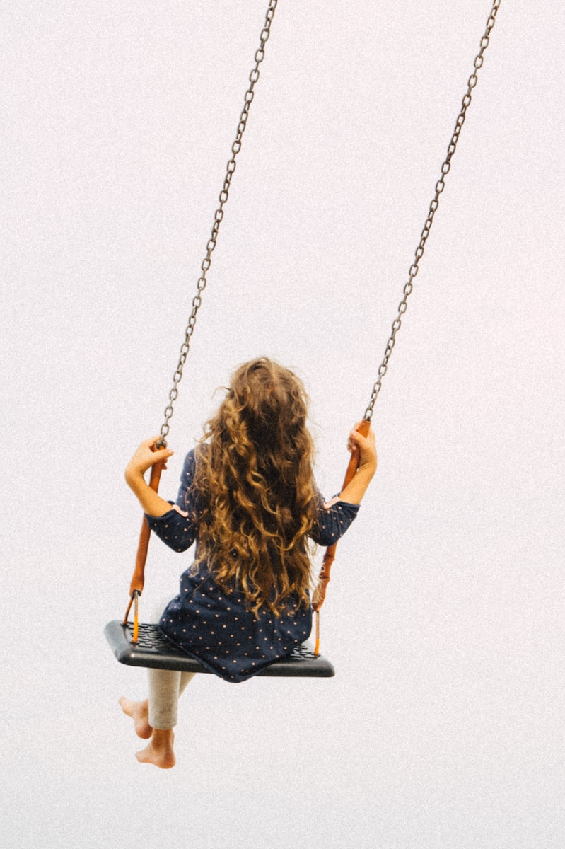 a little girl sitting on a swing in the air